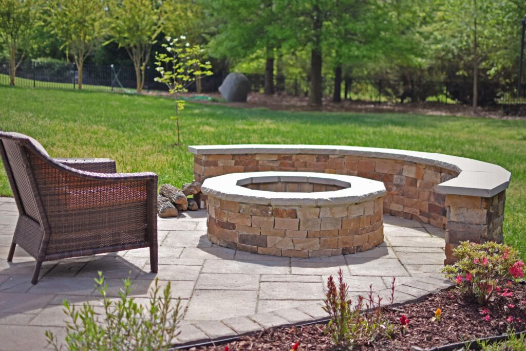 A stone fire pit with blue glass crystals inside. There is a stone wall to sit around it and also an elegant stone floor that makes the whole set combine. Outdoor experience.
