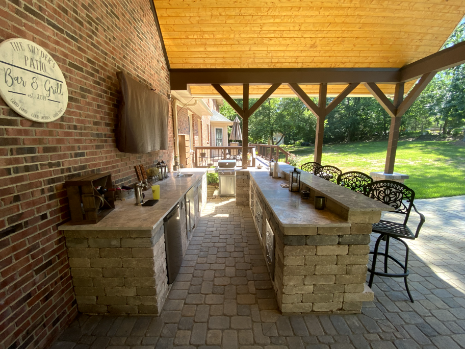 An amazing stone outdoor kitchen decorated with metal chairs. It's being covered by a wooden roofing.