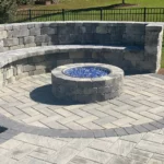 A stone fire pit with blue glass crystals inside. There is a stone seating walls to sit around it and also an elegant stone floor that makes the whole set combine.
