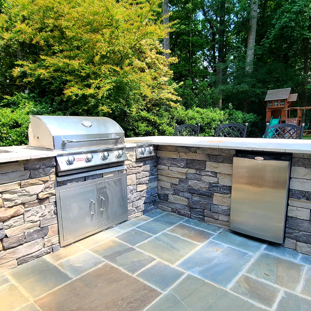 A metal outdoor kitchen with a little fridge, embeded in a stone deck. A lot materials blend in this photo.