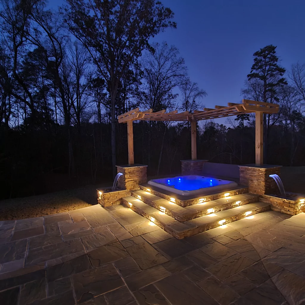 A pergola (only half) with a hot tub below. It's nighttime and the hot tub has a set of lights that changes colors.