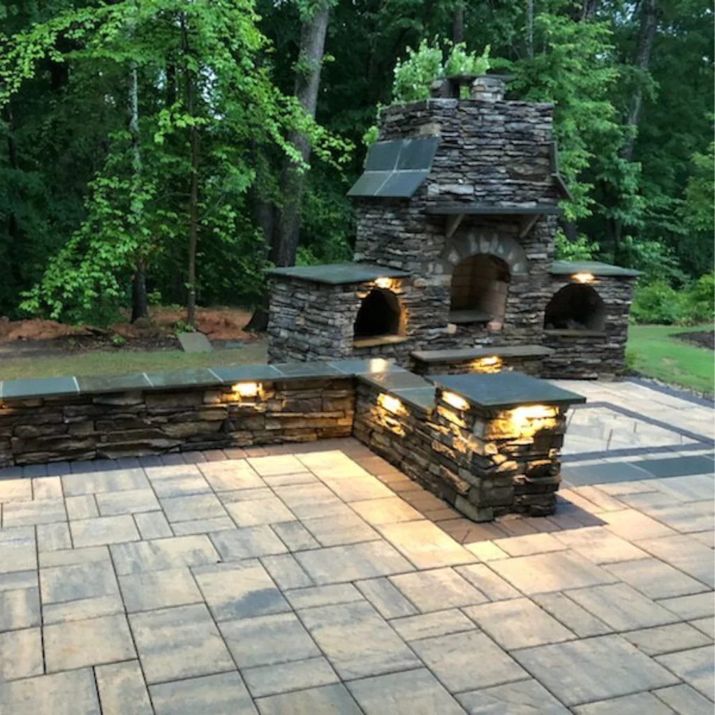 An outdoor fireplace built in stone with a greenish forest in the background.