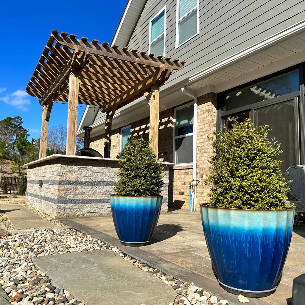 A wood pergola on a little rock wall. There are some large ceramic pots adorning the patio.
