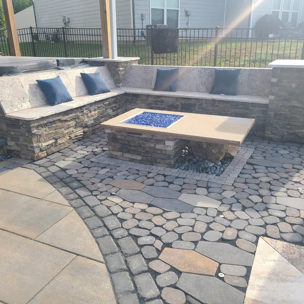 A stone fire pit in a patio. There's a concrete L shape sofa with cushions on it.