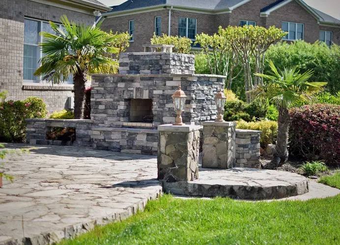 An outdoor fire place in a patio. It has a nice stone floor and plants around it.