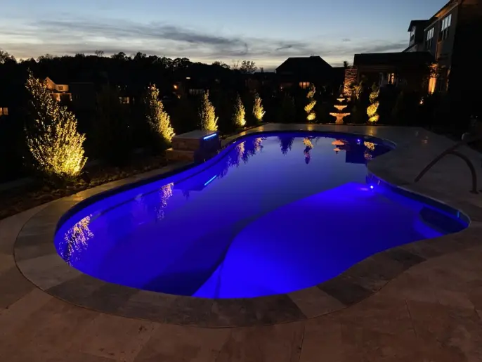 A pool with lights and a cascade at dawn. There's also a fountain and outdoor lighting in the patio.