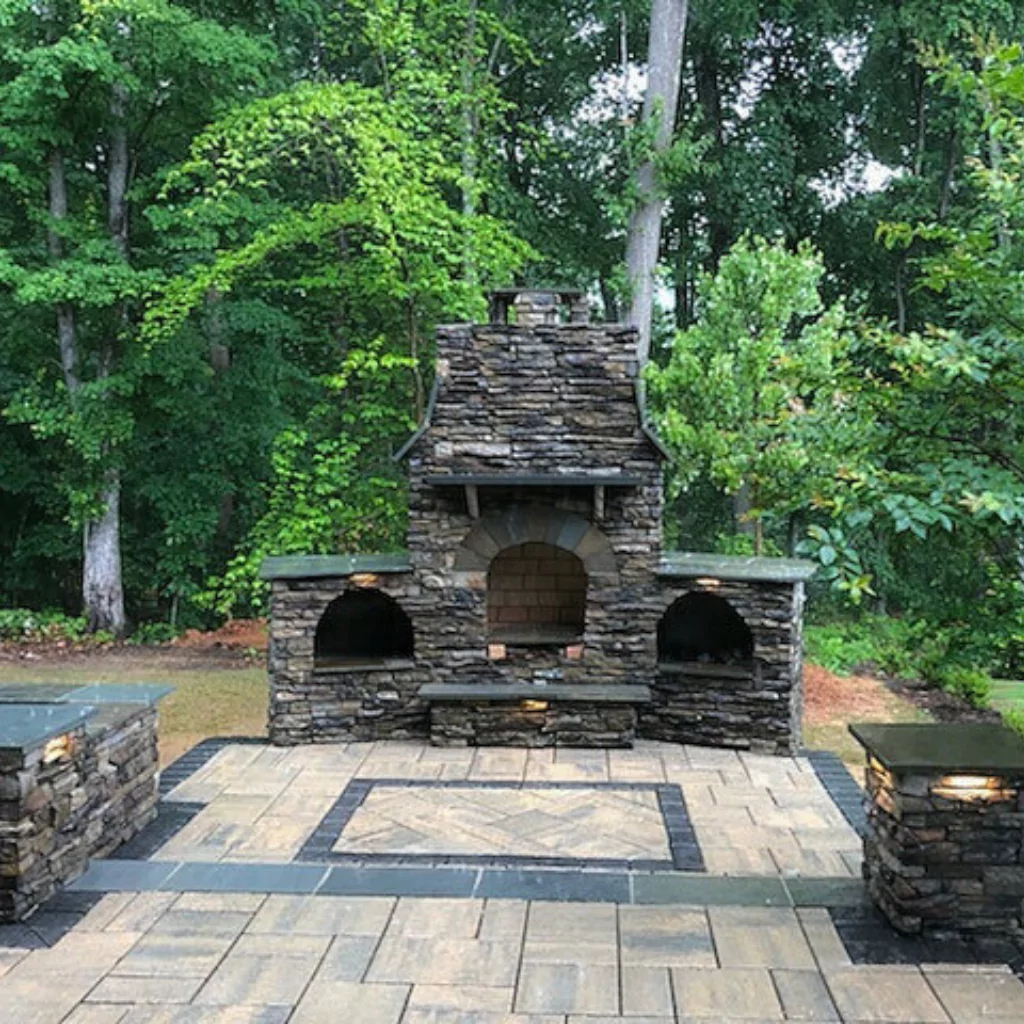 An outdoor fireplace built in stone with a greenish forest in the background.