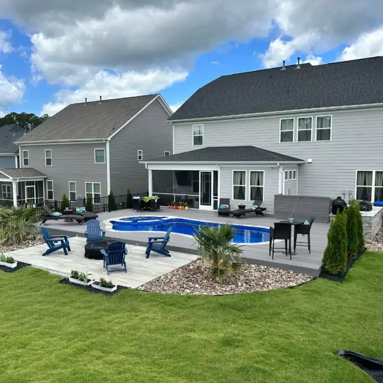 A beautiful patio with a swimming pool. There is grass all around and some outdoor chairs. An outdoor living space