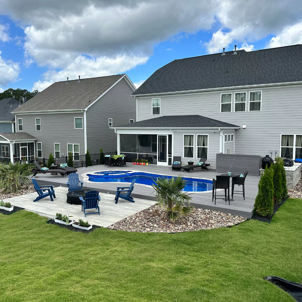 A beautiful patio with a swimming pool. There is grass all around and some outdoor chairs.