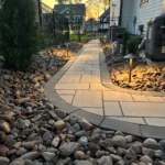 A path of stone slabs leading to the entrance of a patio. The path is decorated with small stones and lights around it.