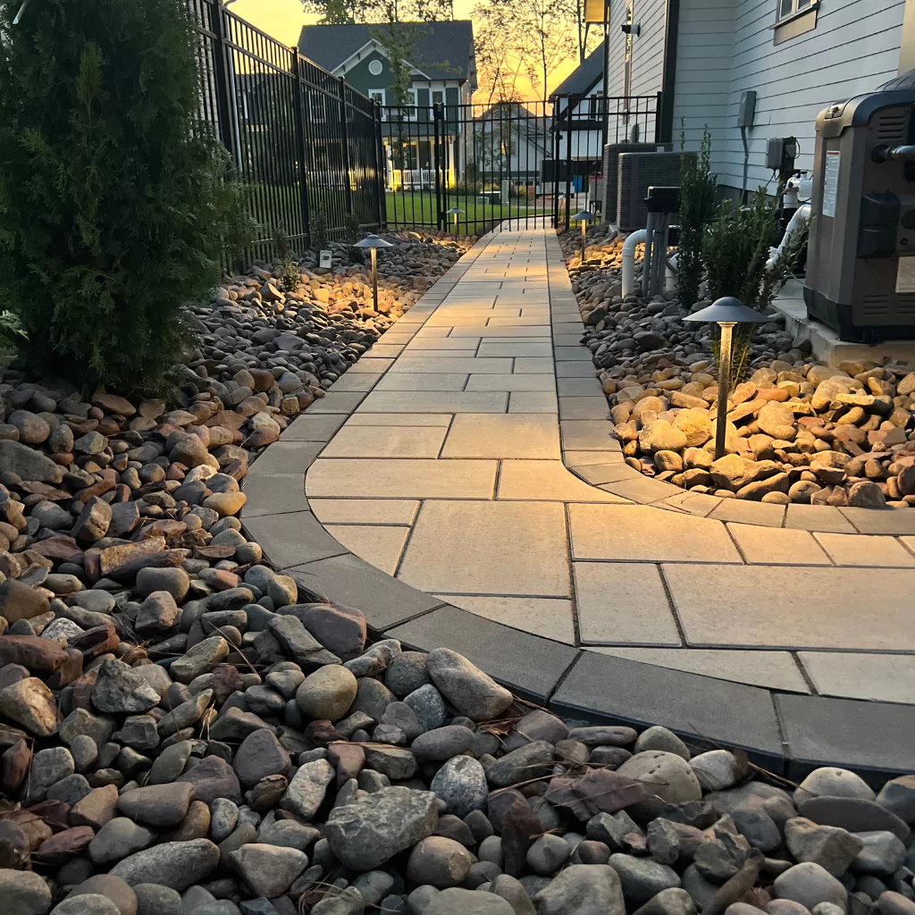 A path of stone slabs leading to the entrance of a patio. The path is decorated with small stones and lights around it.