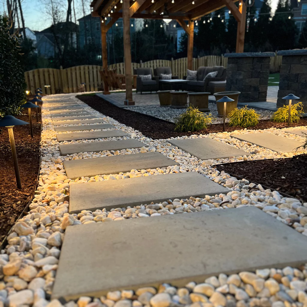 Big stone tiles that leads a way to a beautiful pergola. Those stone tiles are surrounded by little rocks.