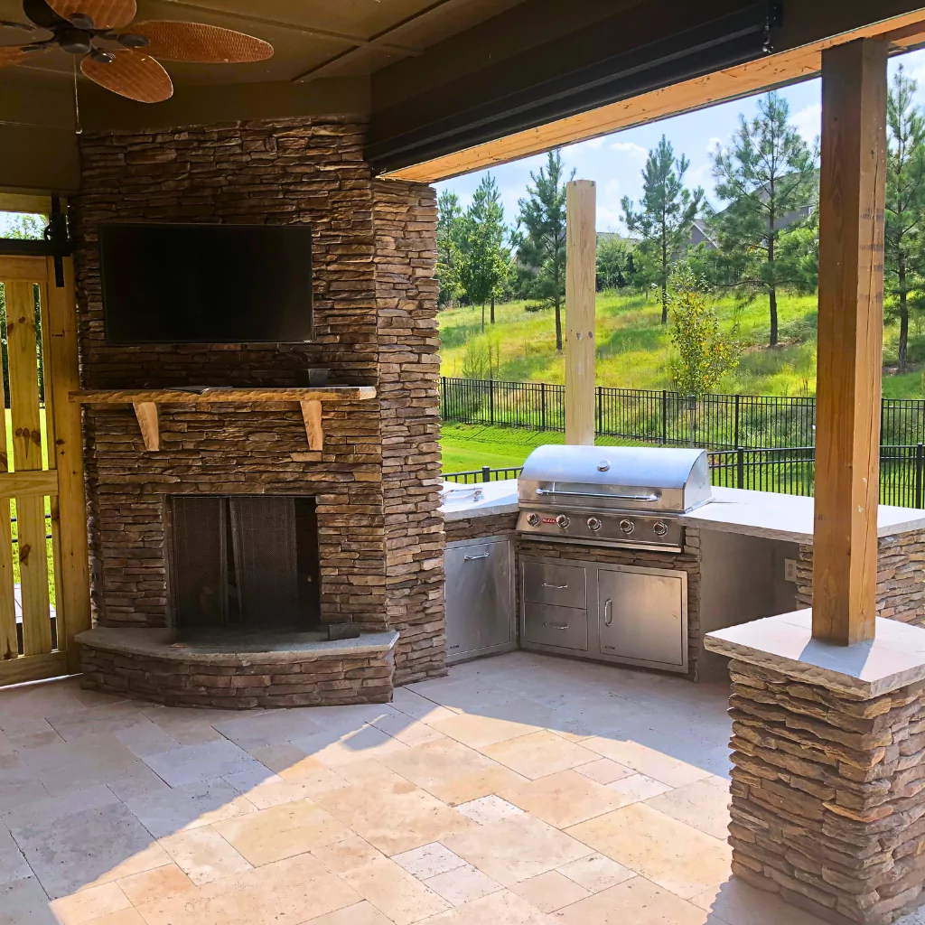 A beautiful outdoor kitchen fitted in stone under a pergola. Nearby there is a fireplace