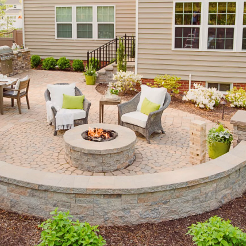 A beautiful patio with a firepit, some winter plants and outdoor furniture. All those elements are surrounded by an elegant hardscape design.