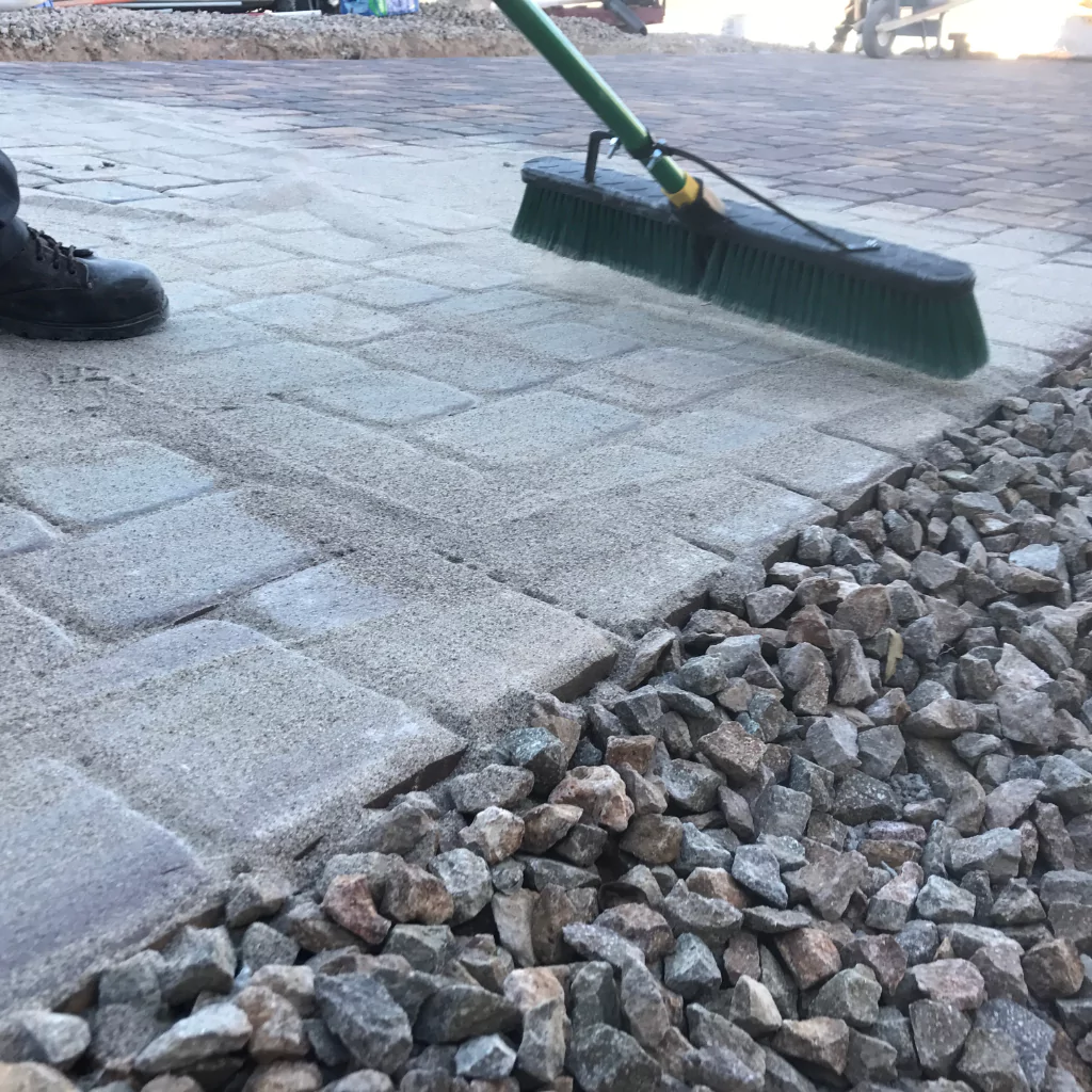 A person cleaning pavers with a broom