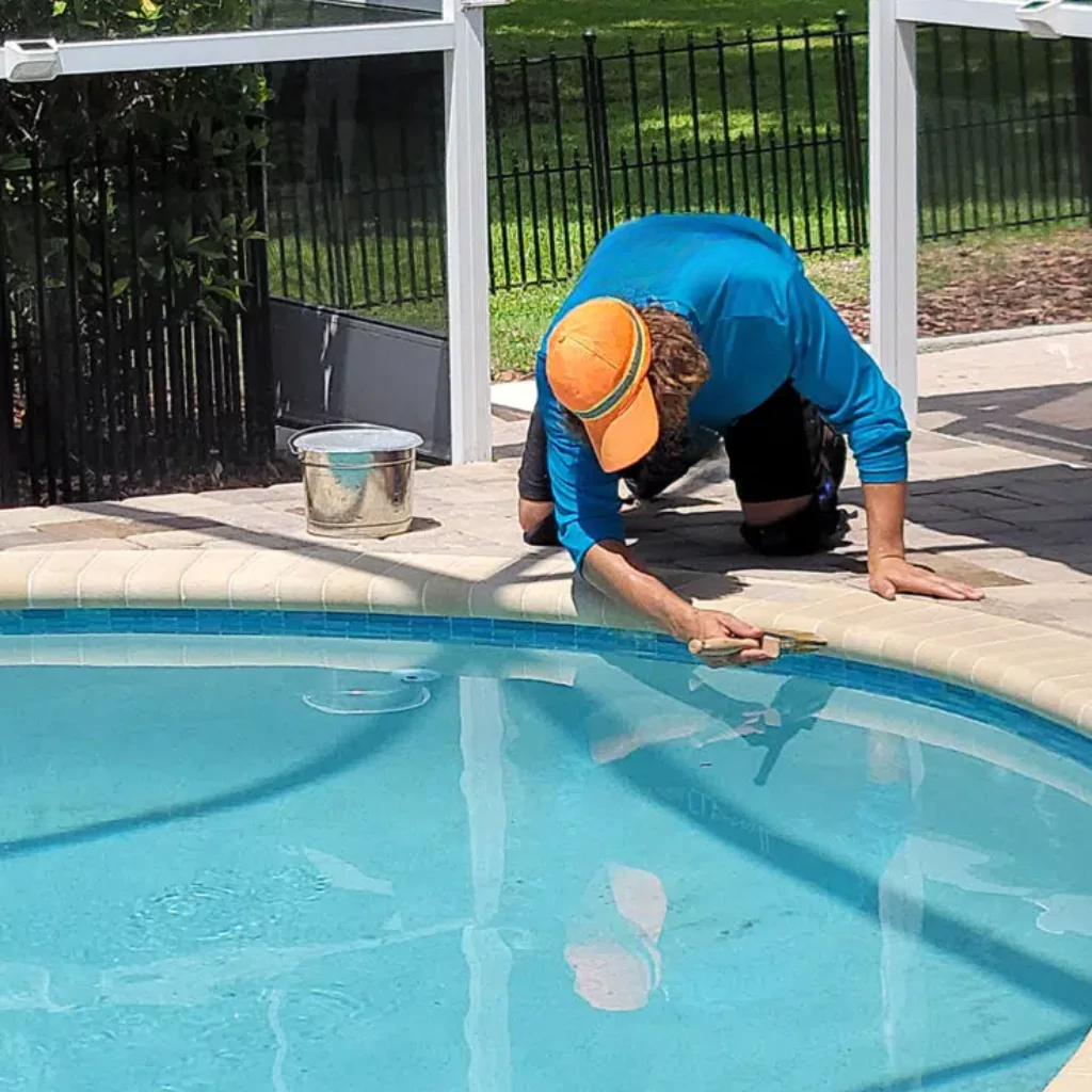 A person doing some maintenance to pavers around a pool
