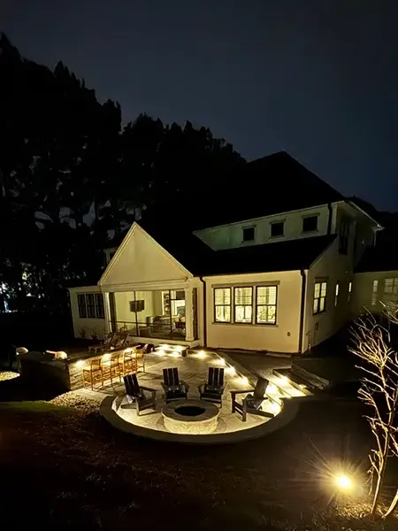 A beautiful stone fire pit decorating a patio along with strategically placed outdoor lights to create an incredible ambiance during the cold nights.