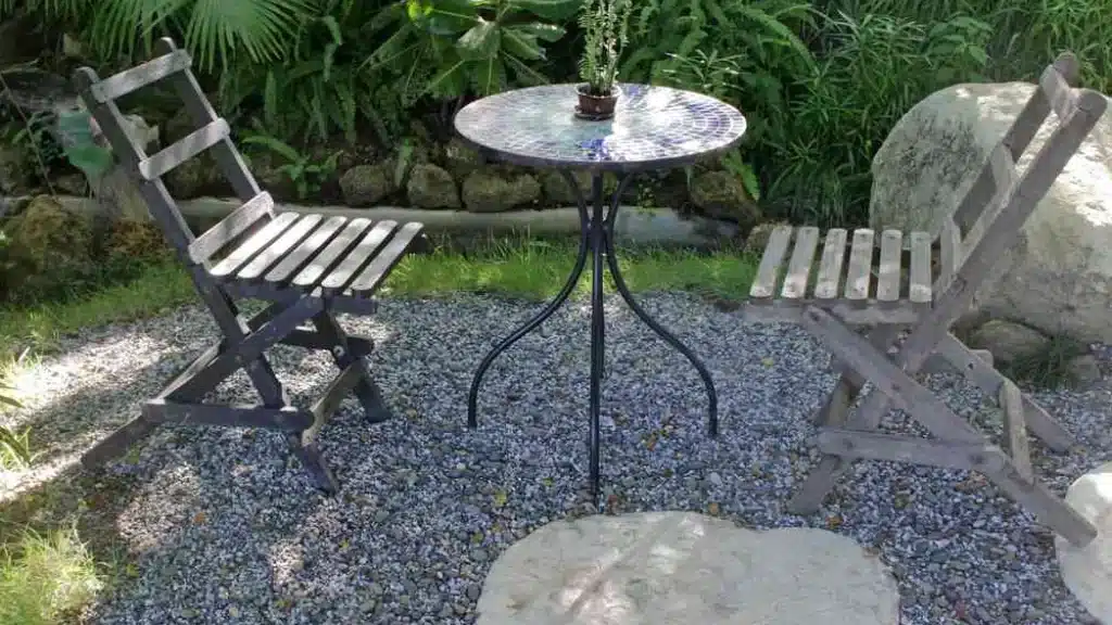 Gravel and stone tiles in a patio. There are steel chairs and a steel table on them.