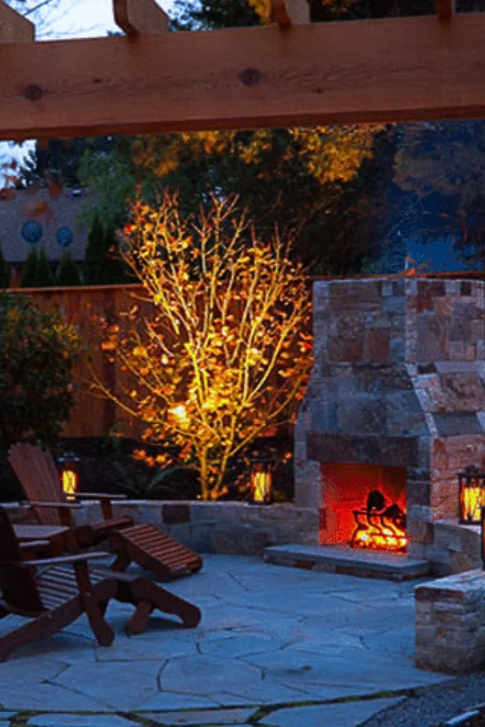 A beautiful stone patio with a pergola and a lit fireplace.