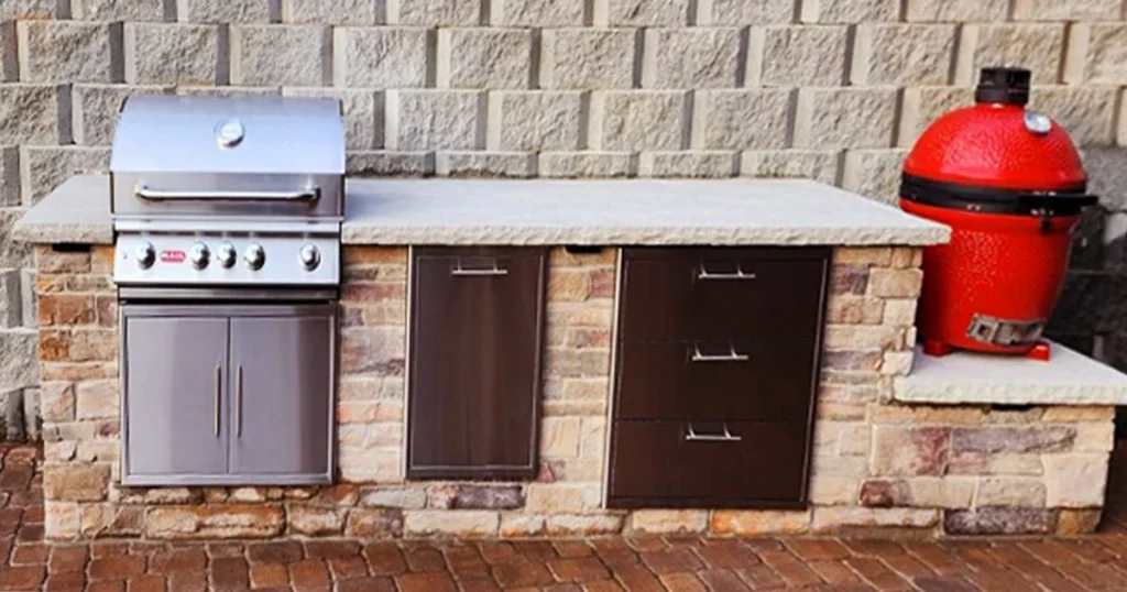 Custom outdoor kitchen by SunSouth Carolinas featuring durable brick masonry base, built-in gas grill, Kamado grill station, storage, and countertop on paver hardscaping.