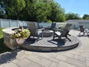 Circular stone fire pit installation by SunSouth Carolinas, featuring contrasting paver patio design and a curved stone seating wall for cozy gatherings