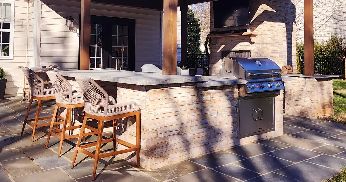 SunSouth Carolinas custom outdoor kitchen featuring built-in grill, stainless steel storage, integrated outdoor bar seating area, and attractive stone masonry base on flagstone hardscaping.