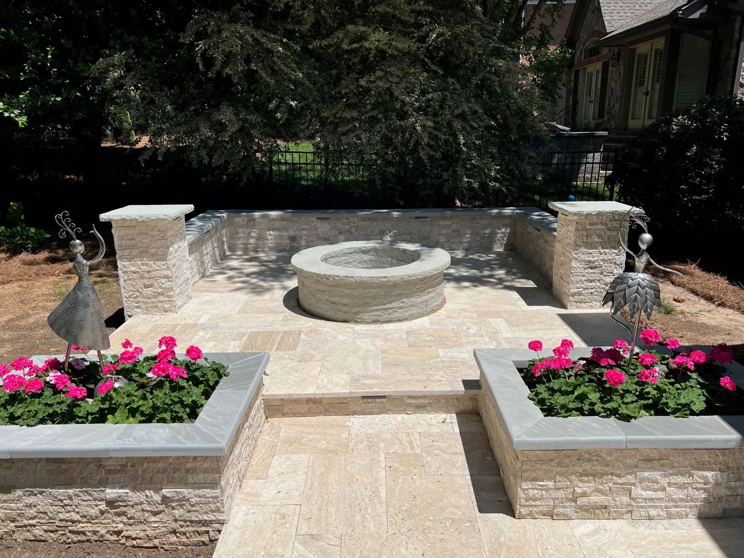 Elegant natural stone patio installation by SunSouth Carolinas featuring a matching stone fire pit, built-in seating wall, and custom stone planters.