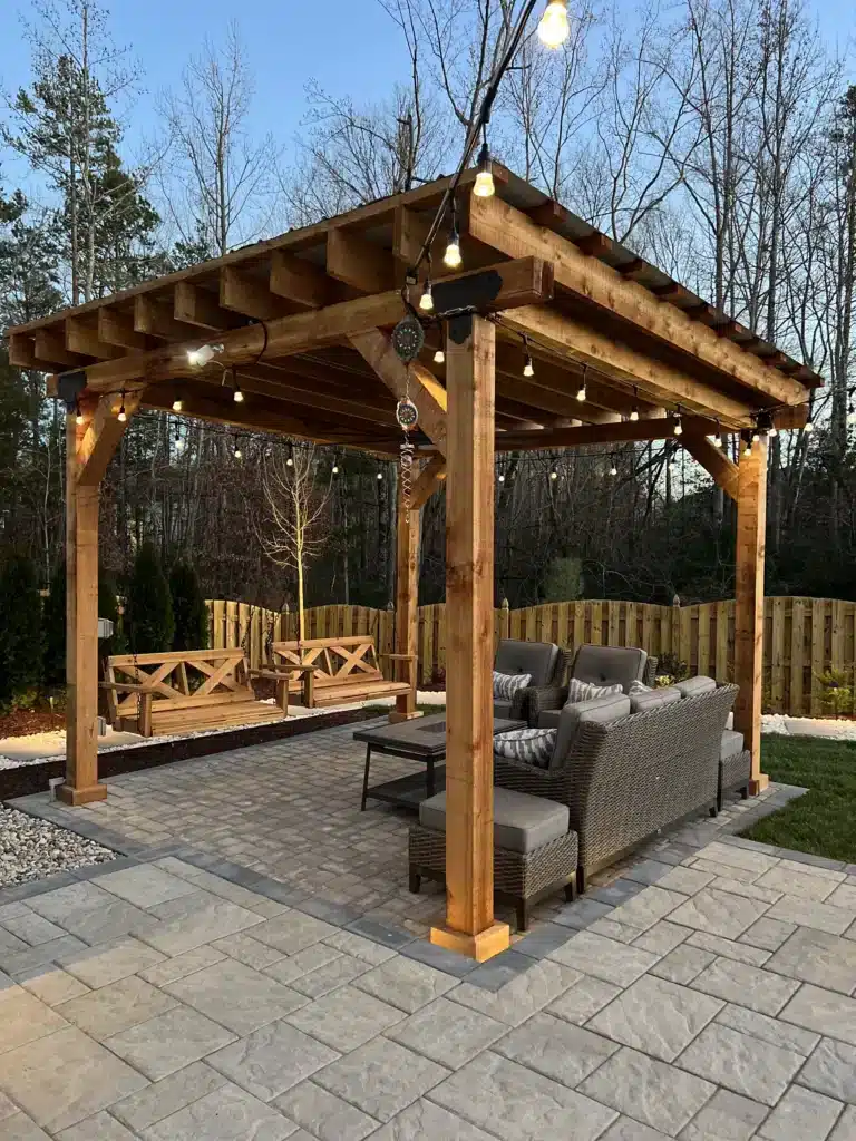 How to Hang Outdoor Lights Without Damaging Your Structures 3 Expansive custom wood pergola by SunSouth Carolinas shelters multiple distinct seating areas on paver hardscaping, enhanced by festive custom outdoor lighting (string lights).