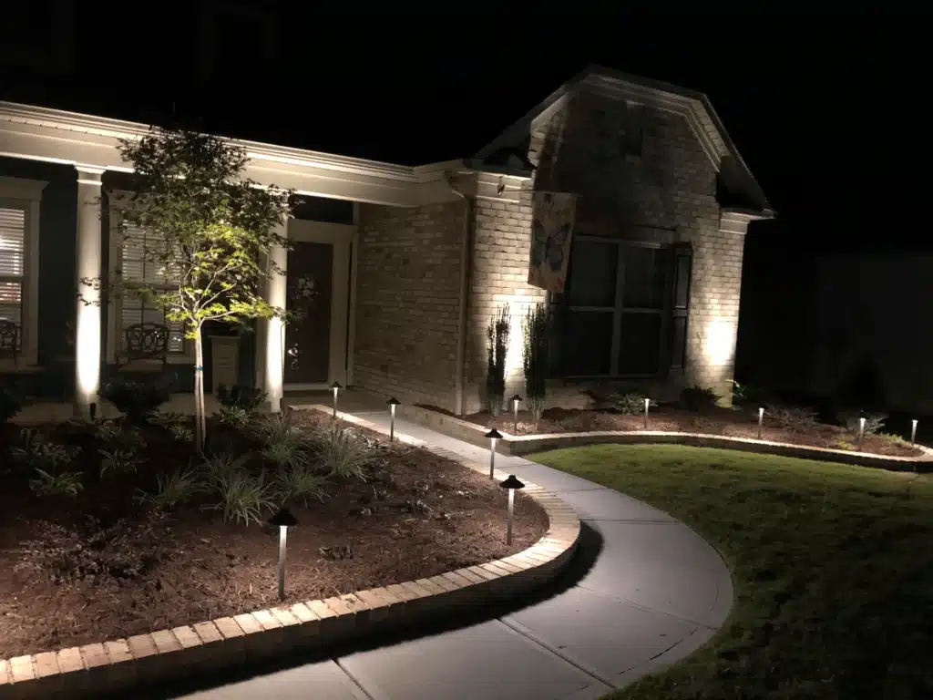 Custom outdoor lighting service by SunSouth Carolinas highlights stamped concrete hardscaping walkway and border landscaping for safe, inviting nighttime entry.