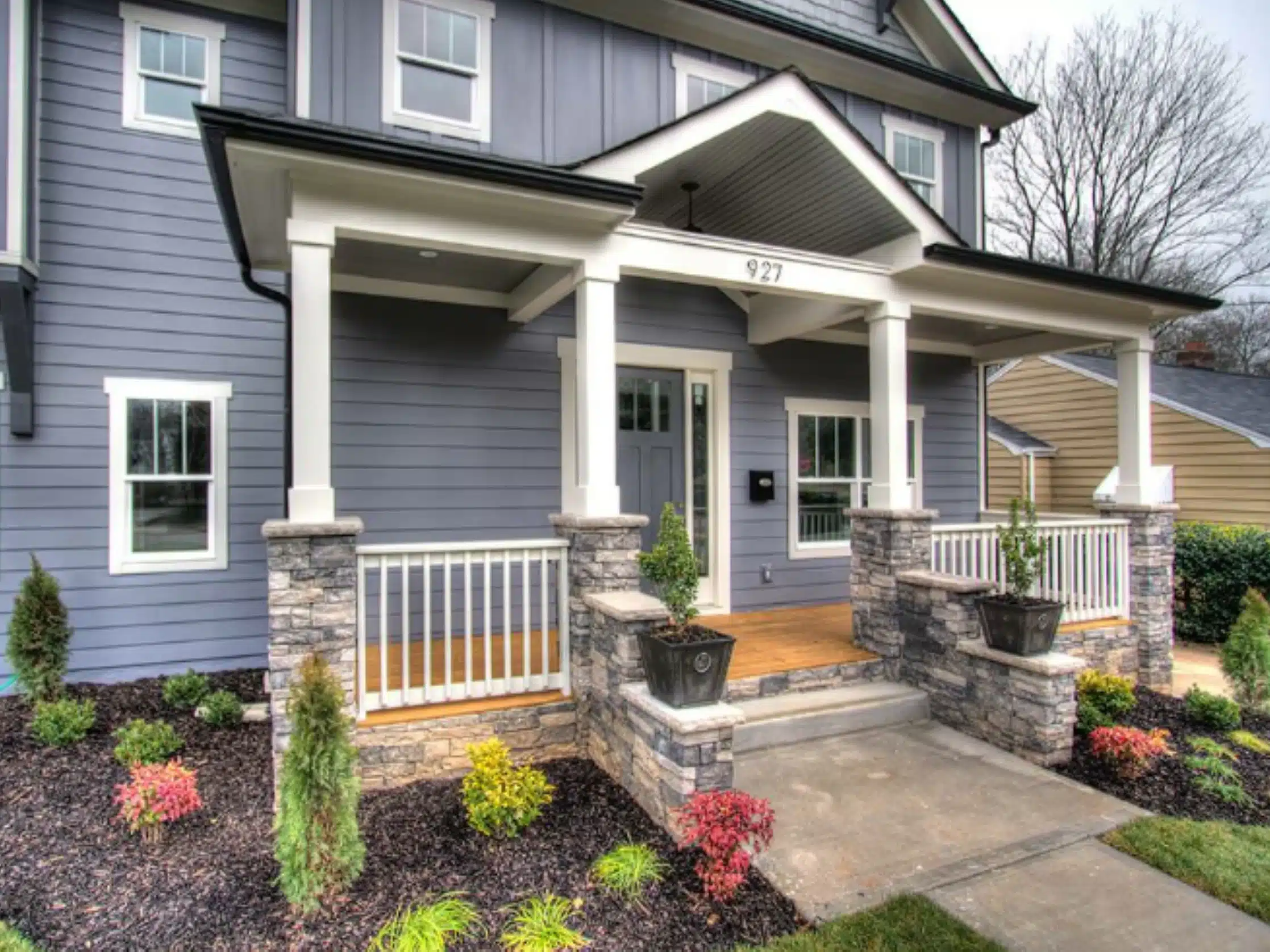 Impressive stone masonry pillars define this inviting front porch design by SunSouth Carolinas, connected by durable hardscaping pathways and bordered by colorful landscaping.