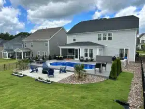 Complete outdoor living space designed by SunSouth Carolinas, featuring a custom fiberglass swimming pool, extensive hardscaping for lounging, covered porch access, and strategic landscaping.
