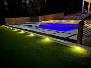 SunSouth Carolinas fiberglass swimming pool installation enhanced with integrated custom outdoor lighting, highlighting the hardscaping, masonry steps, and landscape design at dusk.