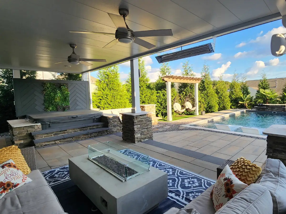 Romantic Outdoor Spaces: Fire Features Designed for Cozy Winter Nights 1 Relaxing on the sofa in a luxurious outdoor living room, complete with a modern fire table, ceiling fans, and a view of the custom hot tub and pool by SunSouth Carolinas.