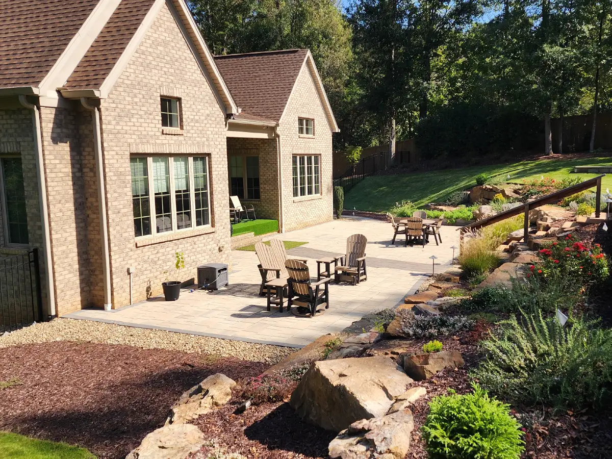 A masterful solution for a sloped backyard, featuring a spacious paver patio and a beautifully landscaped, terraced hillside with stone retaining walls by SunSouth Carolinas.