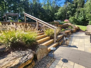 A masterful landscape design for a sloped yard in Charlotte, featuring wide stone steps, lush ornamental grasses, and integrated landscape lighting for beauty and safety.