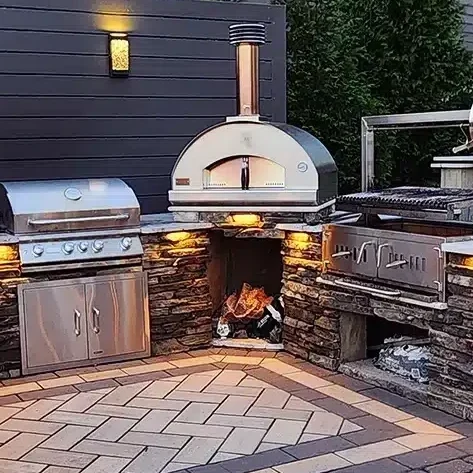 Luxury hardscaping project includes this stunning custom outdoor kitchen installation by SunSouth Carolinas, showcasing beautiful stone masonry, specialty pizza oven, and accent custom outdoor lighting.