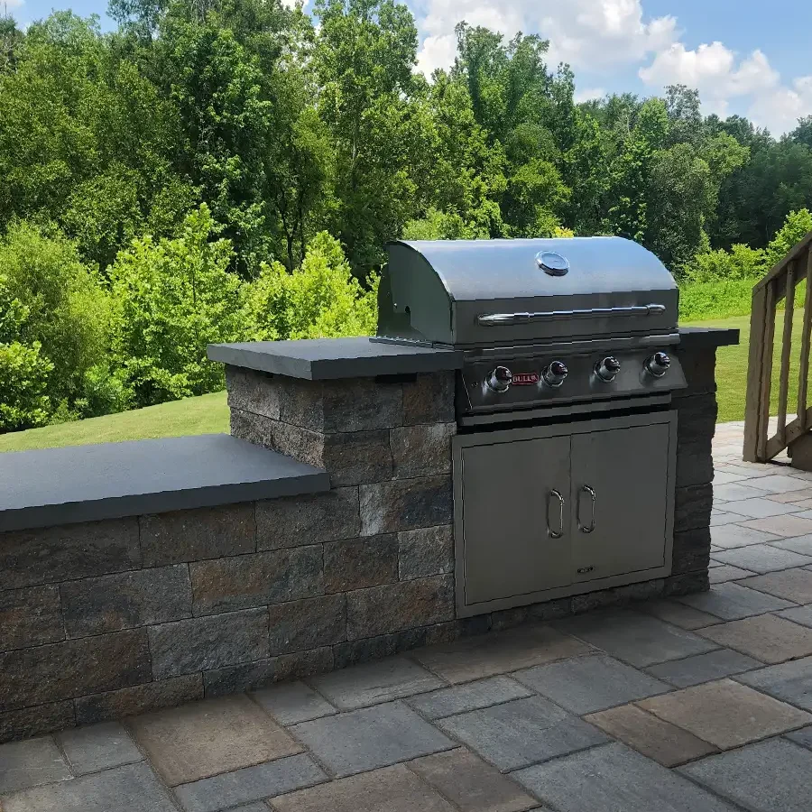 A custom-built outdoor grill station with durable stone block construction, dark countertops, and a high-end built-in stainless steel grill on a paver patio by SunSouth Carolinas.